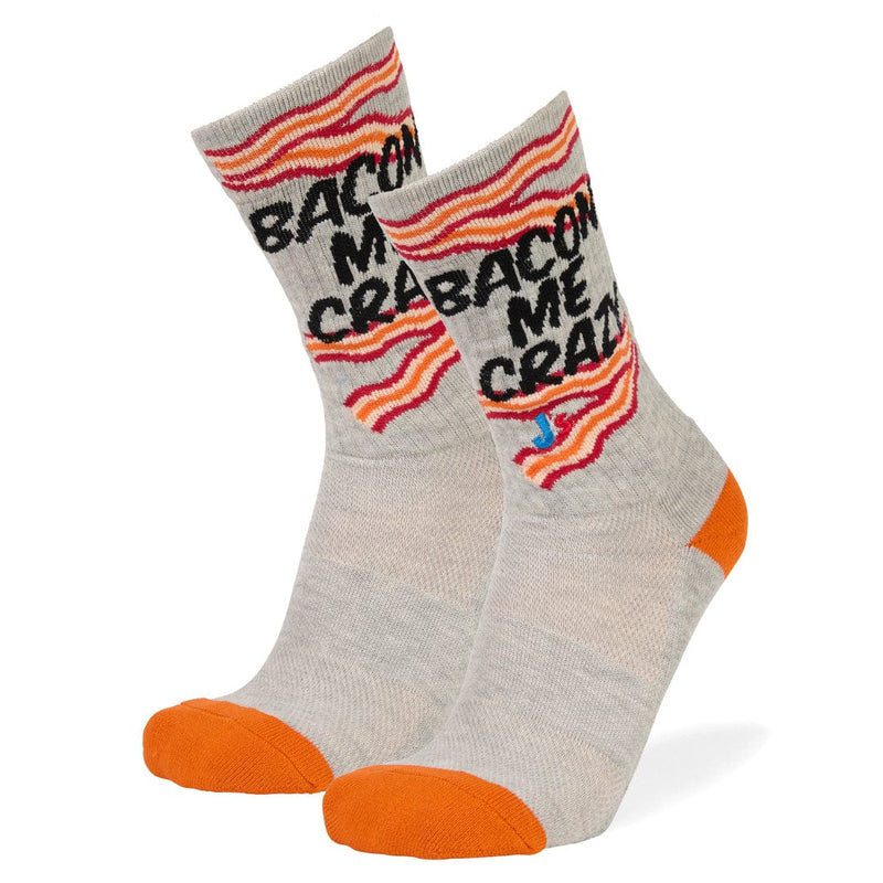 A pair of crew socks in heather gray with orange toes and heels, featuring a bacon-themed design with the text 'BACON ME CRAZY' and striped bacon graphics in red, orange, and yellow.