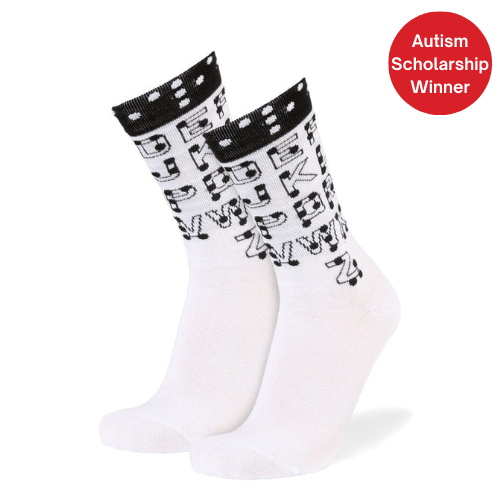 A pair of white crew socks with a black patterned cuff and black lettering across the leg, shown on a white background with a red circular badge that reads 'Autism Scholarship Winner'.