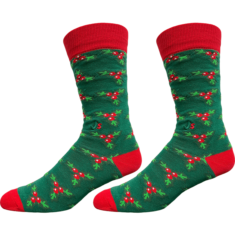 A pair of crew socks with a green background patterned with red berries and green holly leaves, featuring solid red cuffs, heels, and toes, shown against a plain white background.