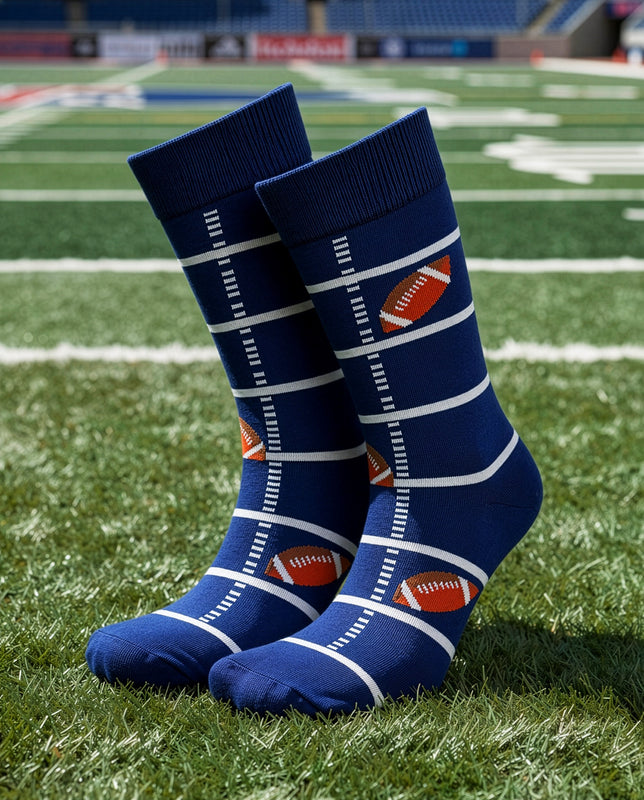 A pair of navy blue crew socks with white yard-line stripes and small orange football graphics, displayed on a green football field.
