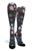 A pair of knee-high socks with a dense floral pattern on a black background, featuring pink, purple, white, and yellow flowers with black toes and heels, shown against a plain white background.